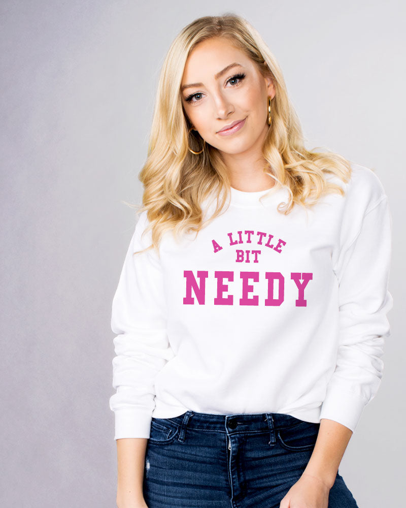 A Little Bit Needy Sweatshirt - Femfetti - A white graphic crewneck sweatshirt with the phrase &quot;A Little Bit Needy&quot; in pink text.