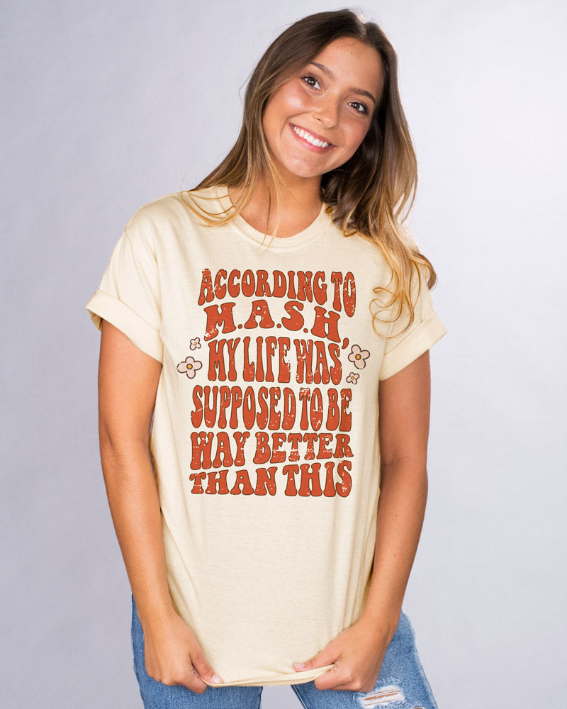 According To MASH - Femfetti - An ivory color unisex fit graphic tee with orange/red text saying &quot;According to MASH my life was was supposed to be way better than this&quot;.