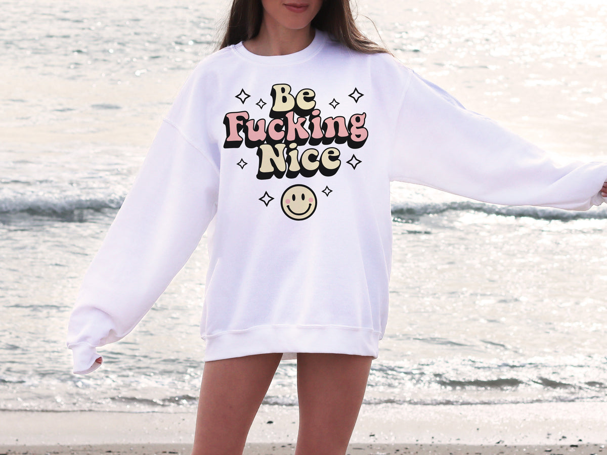 Be Fucking Nice Sweatshirt - Femfetti - A white oversized unisex fit graphic sweatshirt featuring the phrase &quot;Be Fucking Nice&quot; with a smiley face graphic.