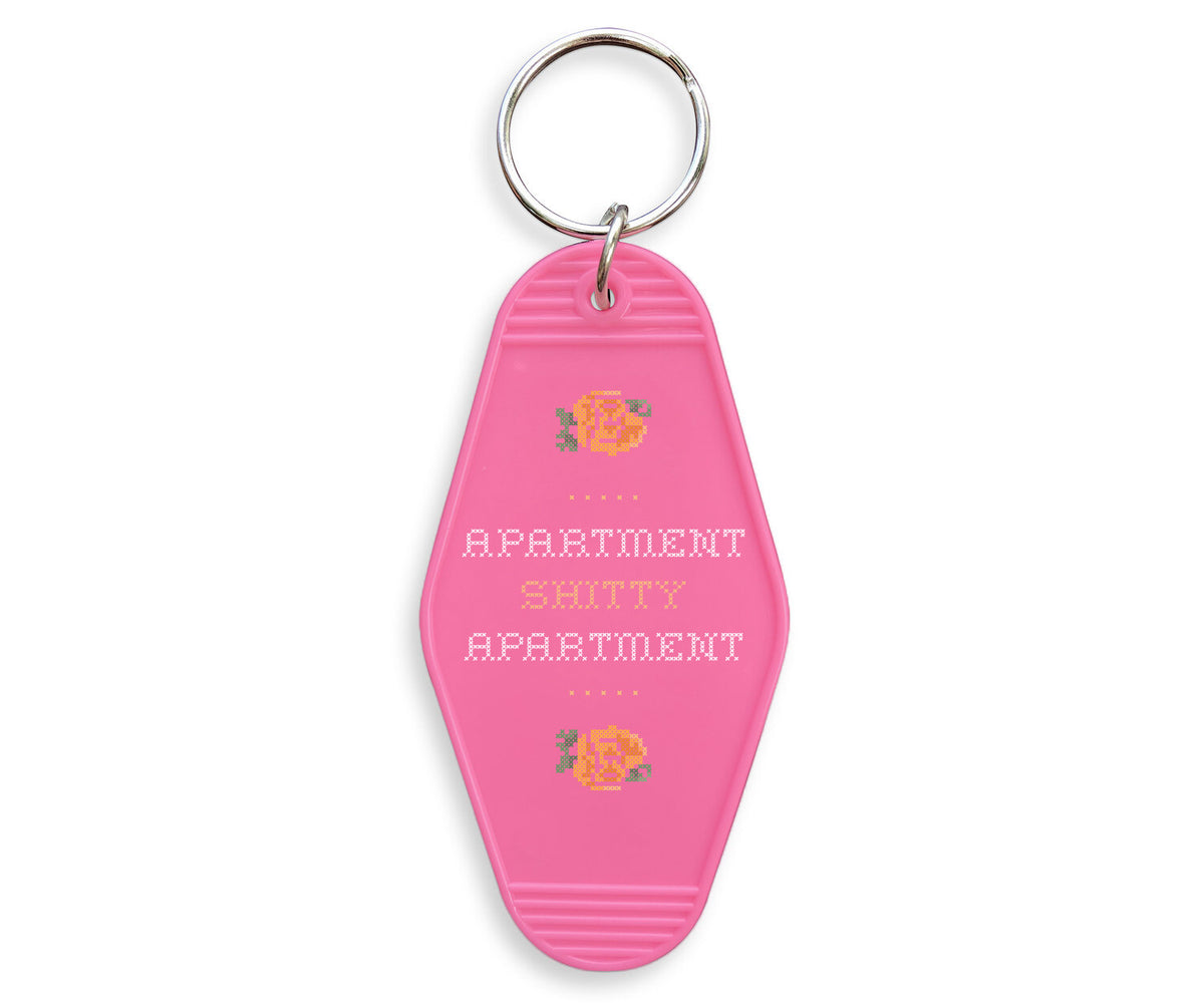 Apartment Shitty Apartment Motel Keychain - Femfetti - A pink retro style acrylic motel keychain featuring the phrase &quot;apartment shitty apartment&quot; in a cross stich style font.