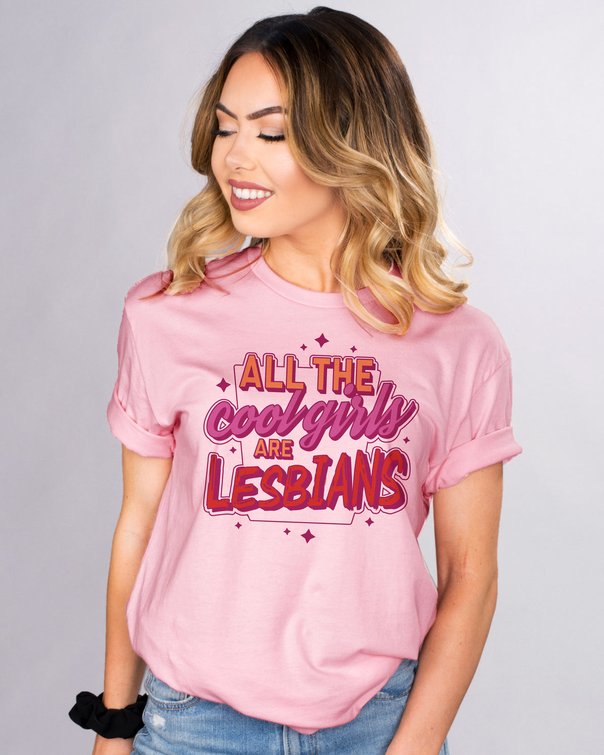 All The Cool Girls Are Lesbians - Femfetti - A pink color unisex fit graphic tee featuring the phrase &quot;all the cool girls are lesbians&quot; in the lesbian pride colors of orange purple and red.