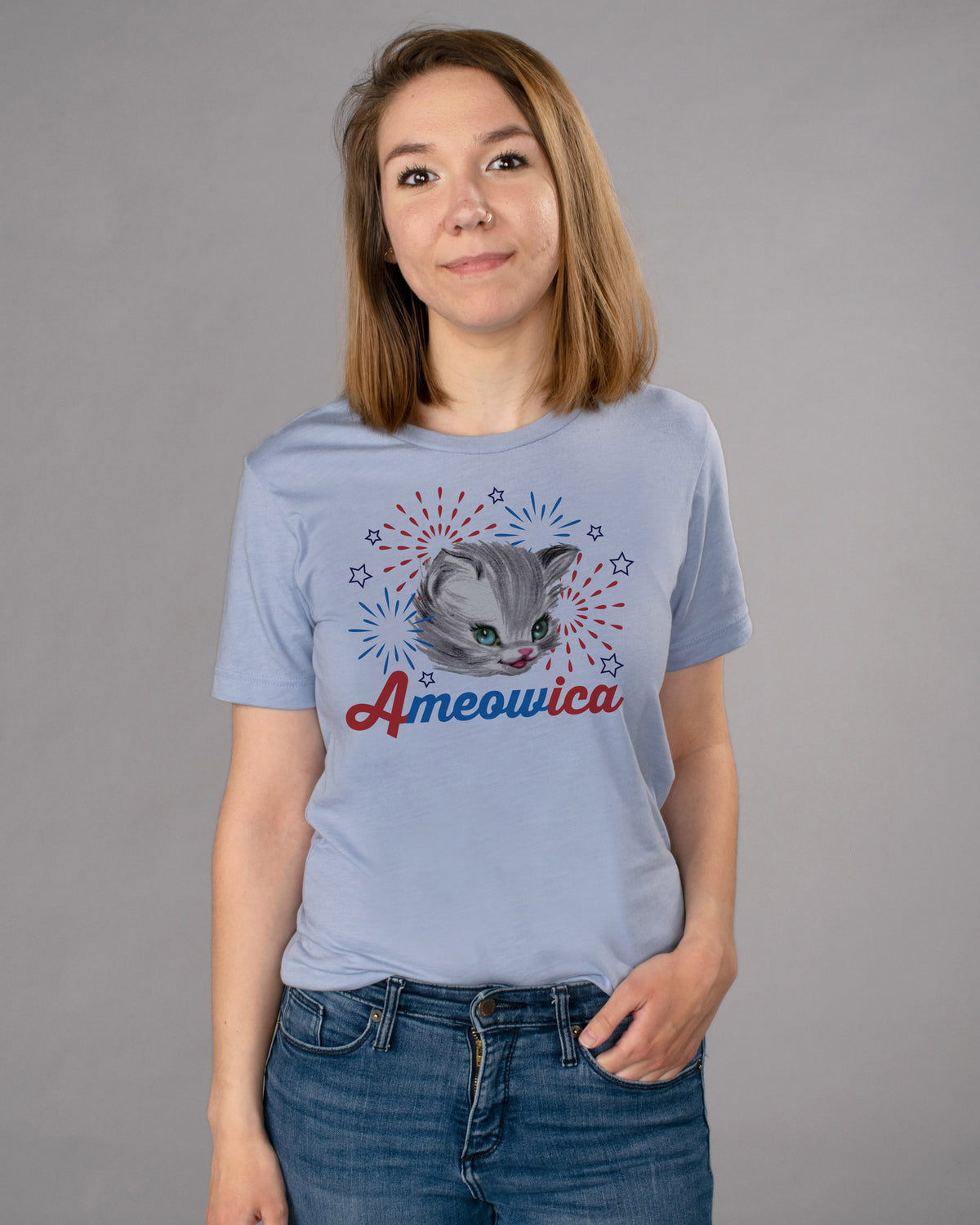 Ameowica Shirt - Femfetti - A light blue unisex fit graphic tee featuring the word &quot;Ameowica&quot; in red and blue with the image of a cat and fireworks.